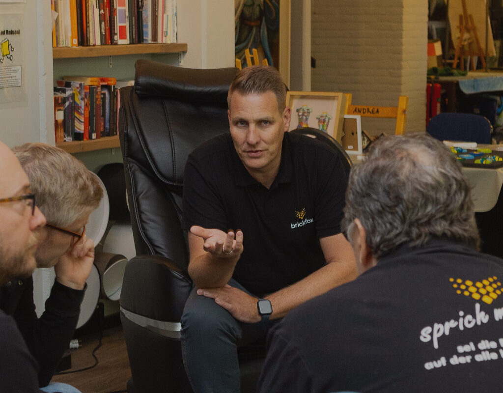 André sitzt auf einen Sessel und diskutiert mit Mehreren.