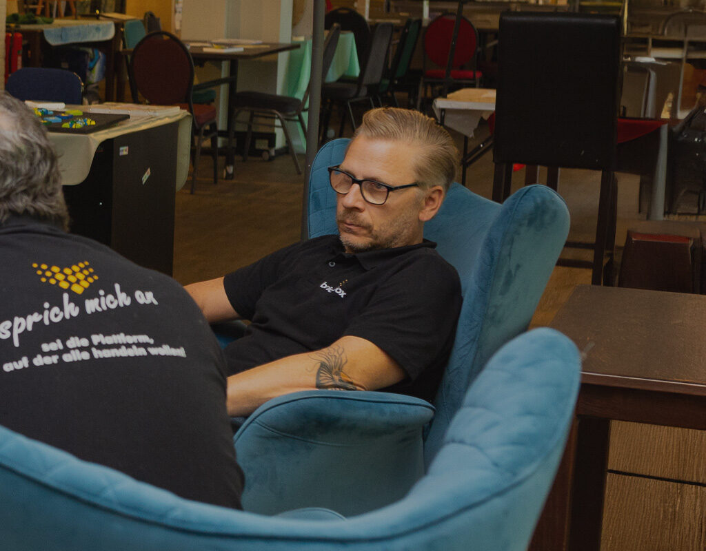 Martin Haak sitzt in einem petrolfarbenen Sessel und schaut in die Gesprächsrunde.