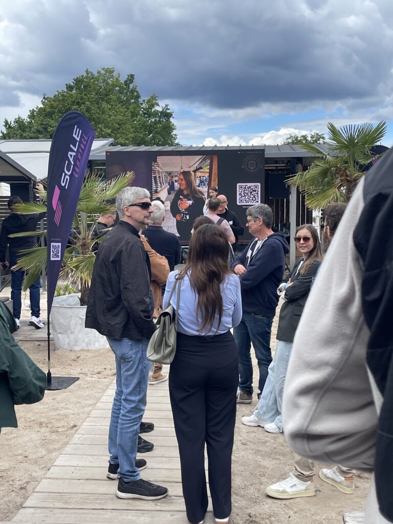 Einige Besucher des BBQ stehen draußen zusammen wo eine Strandatmosphäre geschaffen wurde.